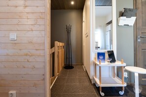 Ein Flur mit einer Holzwand, einer schwarzen Stehlampe, einem weißen Rollwagen mit einem Laptop und einem weißen Waschbecken.
