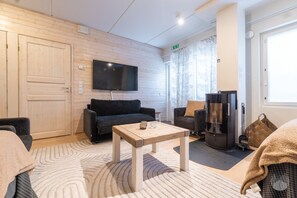 Ein modernes Wohnzimmer mit einem Flachbildfernseher, zwei Sofas, einem Couchtisch und einem großen Fenster mit Vorhängen.