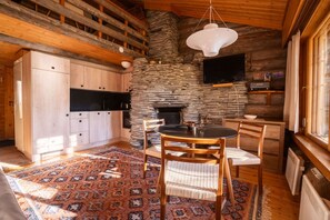 A rustic cabin interior with a stone fireplace, wooden dining table, and a flat-screen TV mounted on the wall. - Levi Pikkurakka 4A3 by Holiday in Lapland (Levi)