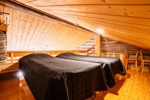 A wooden cabin with a sloped ceiling, two beds with dark bedding, a stone wall, and wooden chairs. - Levi Pikkurakka 4A3 by Holiday in Lapland (Levi)