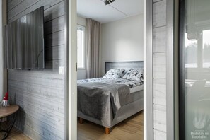 Quarto moderno com cama, televisão de tela plana na parede e janela com cortinas.