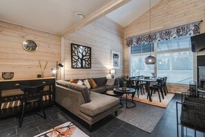 Moderni olohuone, jossa on sohva, ruokapöytä ja tuoleja. Huoneessa on takka, kello ja ikkuna, jossa on sälekaihtimet.