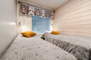 A room with two beds, a window with blinds, a curtain, and a wooden wall. - Levihovi 6B by Holiday in Lapland (Levi)