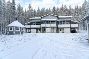 A multi-story building with a central entrance, surrounded by snow-covered trees. - Levihovi 6B by Holiday in Lapland (Levi)