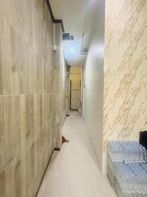 Un couloir aux murs et au sol recouverts de carreaux, et doté d’un luminaire au plafond.