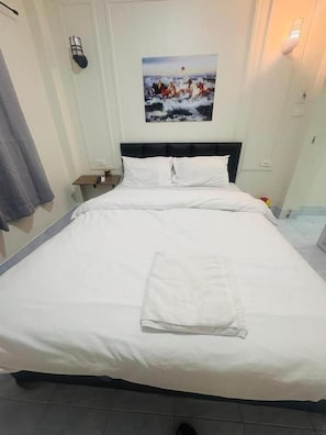 Un lit bien fait, avec du linge de lit blanc et une serviette pliée, une table de chevet avec une lampe et un tableau représentant des chevaux accroché au mur.