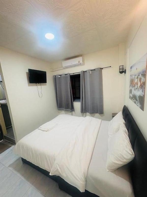 A bedroom with a bed, a flat-screen TV mounted on the wall, a ceiling light, and a painting on the wall. - Hotel Rajputana Residency (Pattaya)
