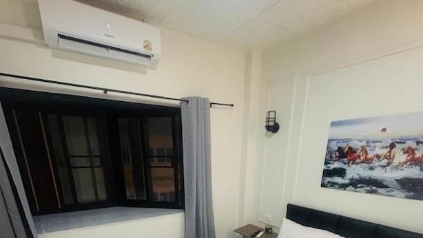 Hotellihuone, jossa on sänky, ikkuna verhoilla, ilmastointilaite ja seinälle ripustettu taulu.