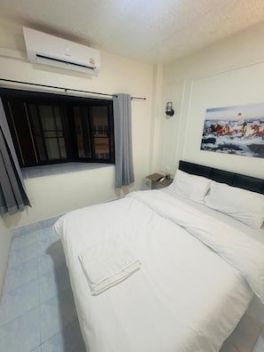 Quarto de hotel com cama, janela com cortinas, ar condicionado e quadro na parede.