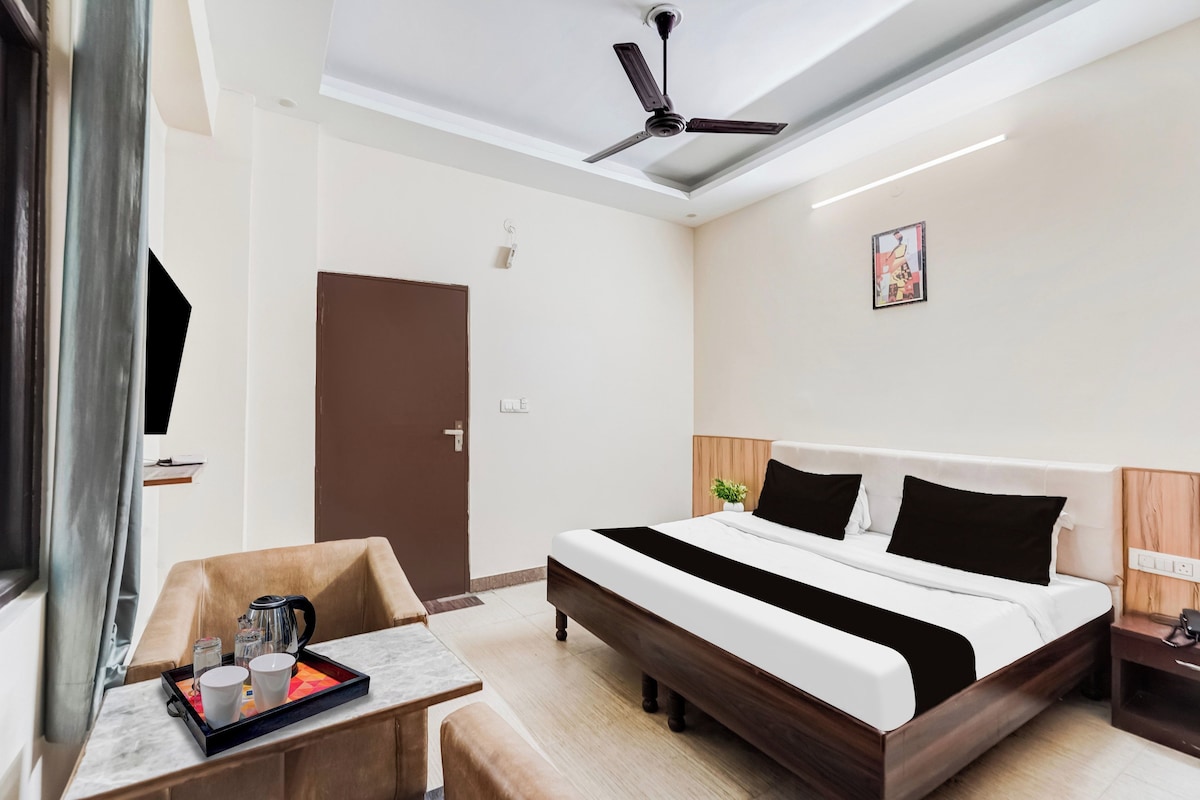 A hotel room with a bed, bedside table, a desk with a tray of items, a ceiling fan, and a door.