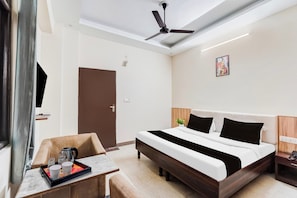 A hotel room with a bed, bedside table, a desk with a tray of items, a ceiling fan, and a door. - Collection O Rispana Pul Dehradun (Dehradun)