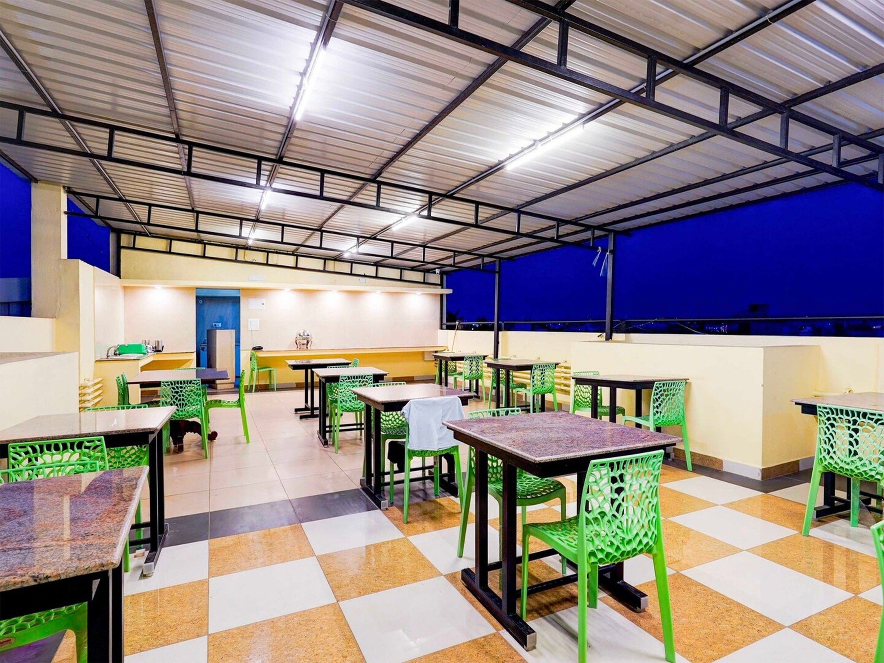 A cafeteria with green chairs and tables, a blue wall, and a tiled floor.