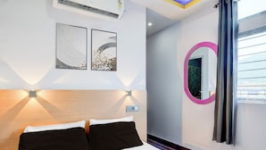 A hotel room with a bed, two wall-mounted artworks, a round mirror, and a window with curtains. - Hotel O Garchuk Market (Guwahati)