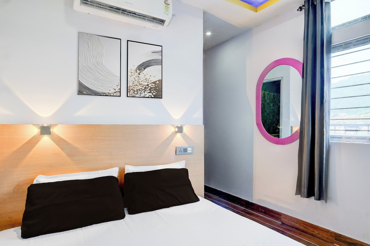 Une chambre d’hôtel avec un lit, deux œuvres d’art accrochées au mur, un miroir rond et une fenêtre avec des rideaux.