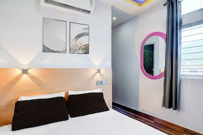 Une chambre d’hôtel avec un lit, deux œuvres d’art accrochées au mur, un miroir rond et une fenêtre avec des rideaux.