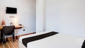 A hotel room with a bed, a desk with a chair, a television mounted on the wall, and a small table with a lamp and a telephone. - Hotel O Garchuk Market (Guwahati)