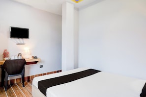 Une chambre d’hôtel comprenant un lit, un bureau avec une chaise, un téléviseur fixé au mur, ainsi qu’une petite table avec une lampe et un téléphone.