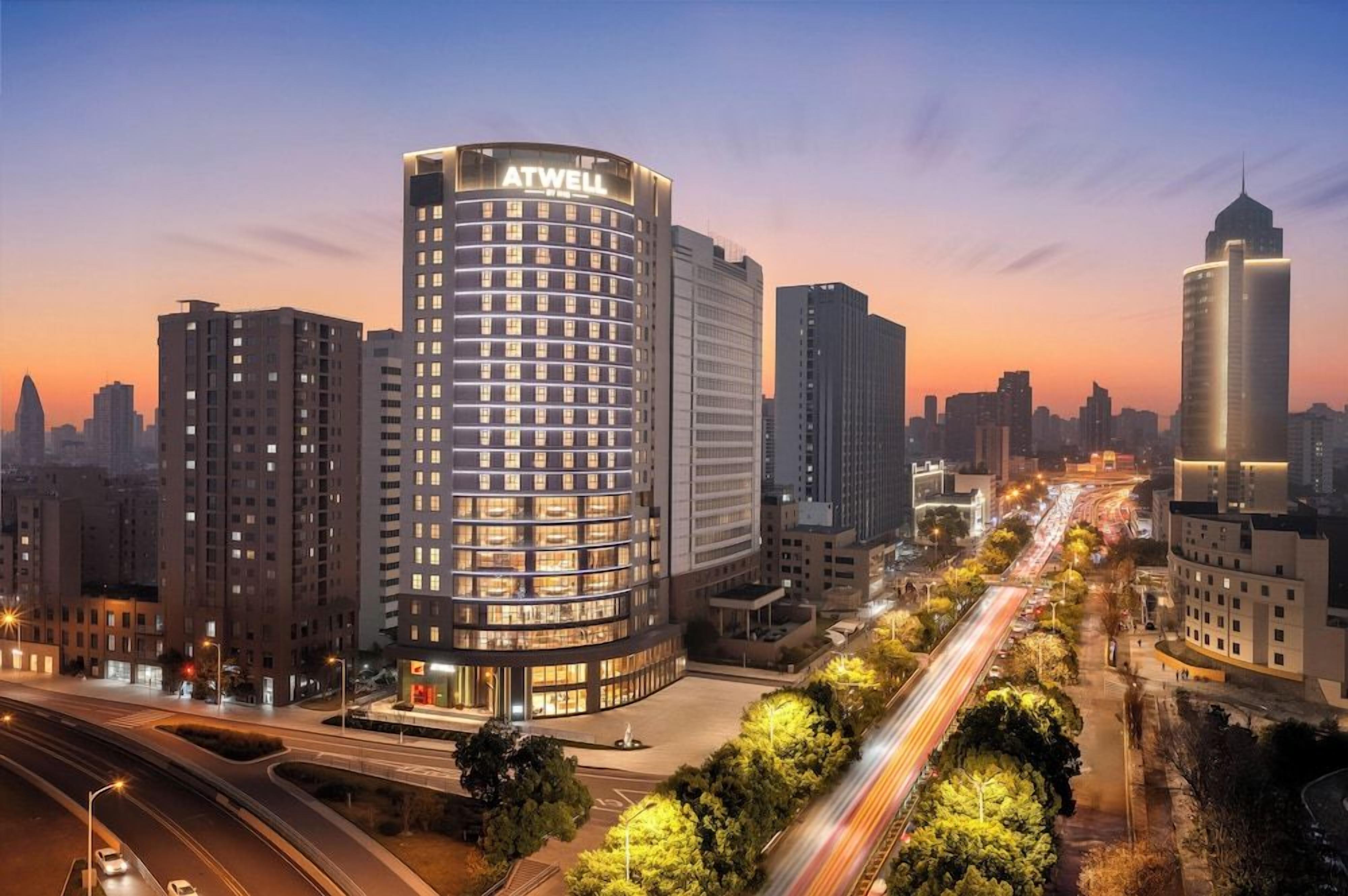 A high-rise hotel with a prominent ATWELL sign, surrounded by other tall buildings and a busy road with light trails.