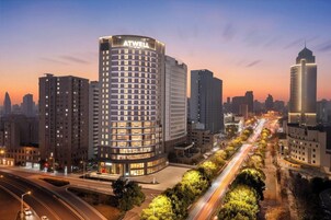Un hotel de gran altura con un llamativo letrero ATWELL, rodeado de otros edificios altos y una calle concurrida con estelas de luz.