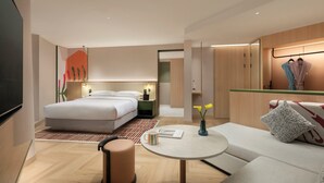 Moderni hotellihuone, jossa on suuri sänky, oleskelualue pöydällä sekä vaatekaappi.