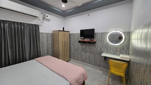 A hotel room with a bed, a wardrobe, a TV, a vanity with a mirror, and a chair. - SRM INN (Ayodhya)