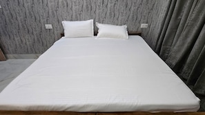 A bed with a white mattress and two pillows, set against a wall with a textured pattern. - SRM INN (Ayodhya)