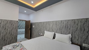 A bedroom with a large bed, a wooden door, and a marble-patterned wall. - SRM INN (Ayodhya)