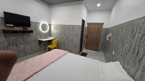 A hotel room with a bed, a desk with a chair, a television, and a door. - SRM INN (Ayodhya)