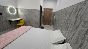 Une chambre d’hôtel avec un lit, un bureau, une chaise, un miroir et une porte.