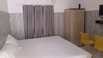 A bedroom with a bed, a wardrobe, a television, and two chairs.