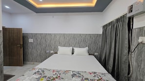 A bedroom with a bed, curtains, a wooden door, and a ceiling light fixture. - SRM INN (Ayodhya)