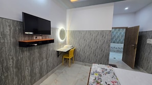 A hotel room with a flat-screen TV, a desk with a chair, a bed, and a door leading to a balcony. - SRM INN (Ayodhya)