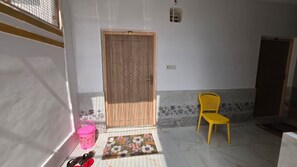 A room with a wooden door, a yellow chair, a pink bucket, and a floral mat.