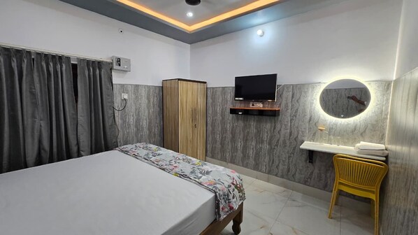A hotel room with a bed, a wardrobe, a television, a mirror, and a small table with a chair.