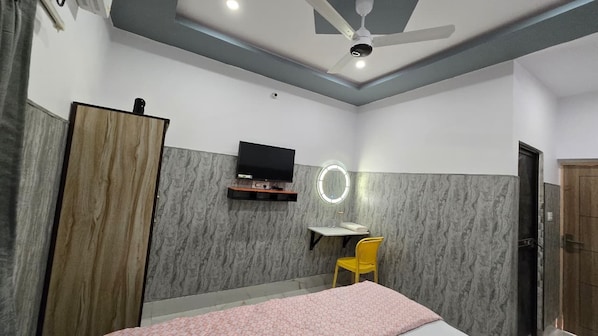A bedroom with a bed, a desk, a chair, a television, and a wardrobe. - SRM INN (Ayodhya)