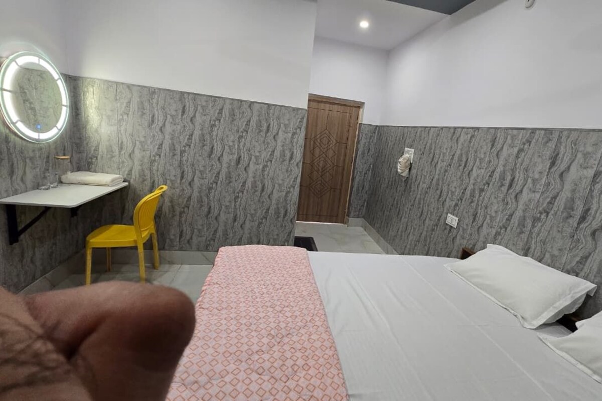A hotel room with a bed, a desk with a chair, a mirror, and a door.