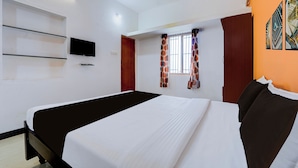 Ein Hotelzimmer mit einem Bett, einem Fernseher, einem Fenster mit Vorhängen und einem an der Wand befestigten Regal.
