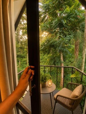 Varanda com cadeira de vime e uma mesa pequena, com vista para um jardim verdejante.