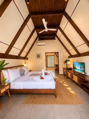 Une chambre avec un plafond en bois, un lit avec une literie blanche, une télévision et une fenêtre avec des stores.