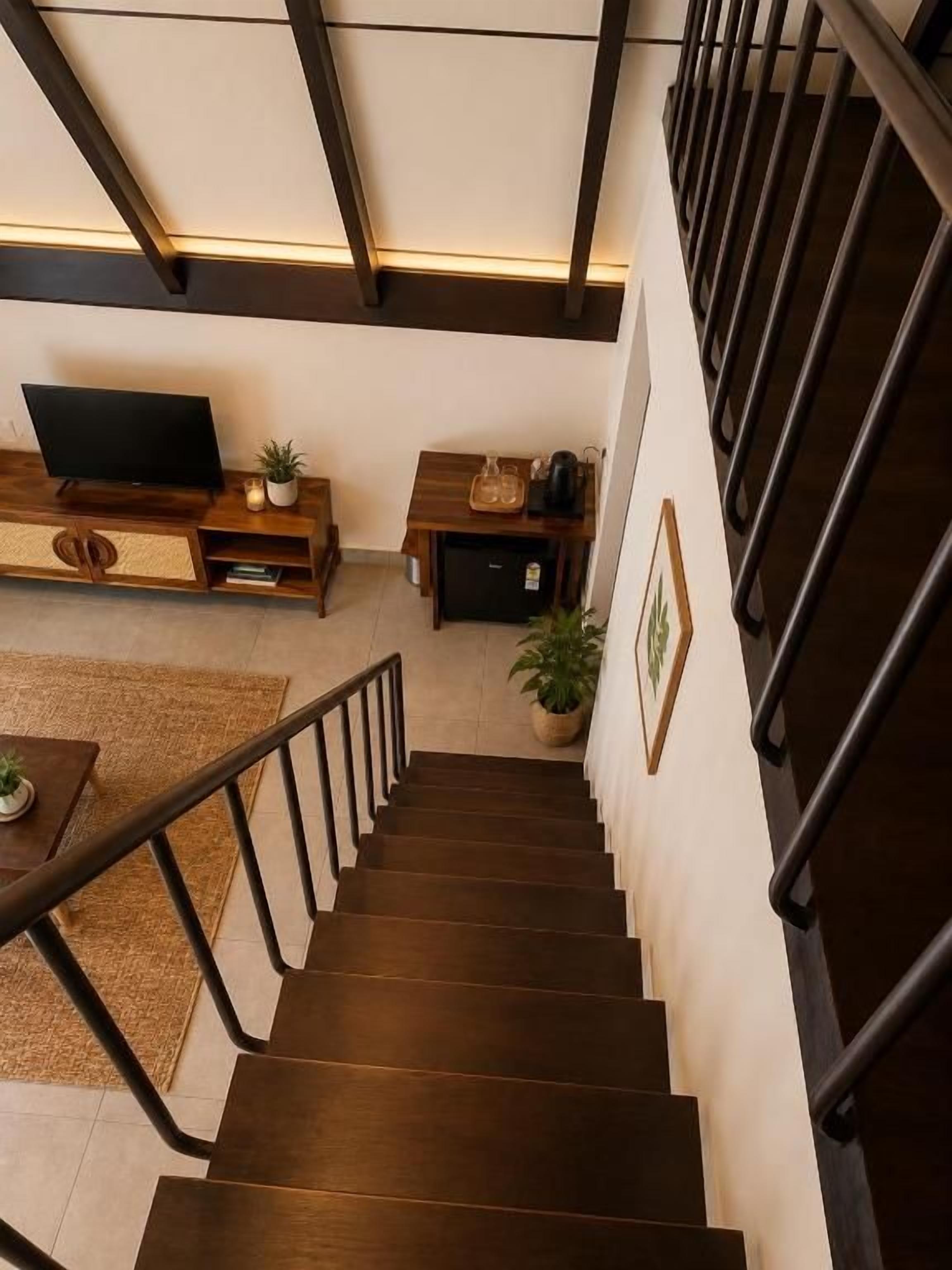 Una escalera conduce a un área de estar con televisor de pantalla plana, muebles de madera y una planta en maceta.