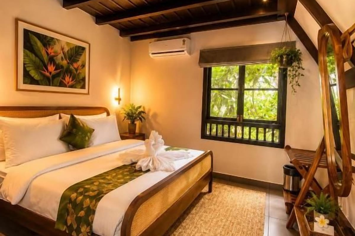 Une chambre avec un lit en bois, une fenêtre donnant sur un beau paysage, un tableau accroché au mur et une plante posée sur le rebord de la fenêtre.
