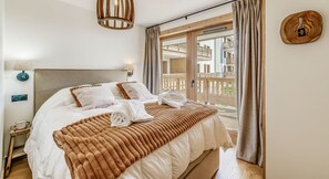 Ein Hotelzimmer mit einem Bett, einem Nachttisch, einer Lampe, Blick auf den Außenbalkon und einer Wanddekoration aus Holz.