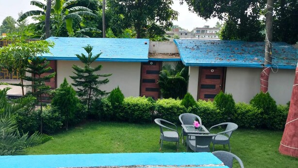 Un hotel con un tetto blu, un piccolo giardino con erba verde e diverse piante, e un tavolo con sedie.