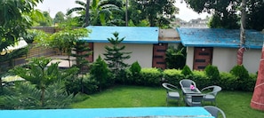 Um hotel com telhado azul, um pequeno jardim com grama verde e várias plantas, e uma mesa com cadeiras.