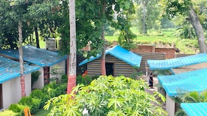 A courtyard with multiple small structures, each with a blue roof, surrounded by lush greenery and trees. - 7 Heaven Hotel & Restro  (Dehari)