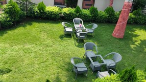 Un'area salotto esterna curata, con mobili in vimini e un tavolino, immersa nel verde e con un pilastro rosso.