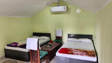 A room with two single beds, a ceiling fan, an air conditioning unit, and a small table with a chair.
