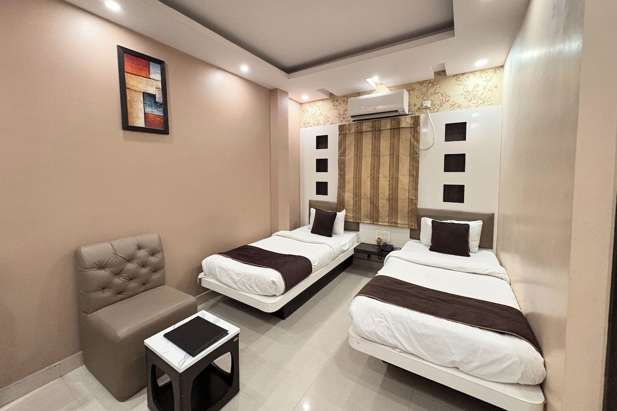 A hotel room with two beds, a sofa, a small table, and an air conditioning unit.