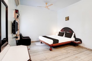 Quarto com cama, escrivaninha, cadeira, ventilador de teto e TV fixada na parede.