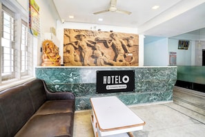 Uma área de recepção de hotel com balcão de mármore, sofá e ventoinha no teto.